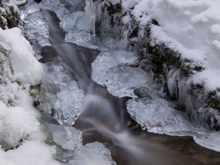 smooth motion of wild water in a river in winter with snow and ice on rocks and stones in the beautiful nature of a forest