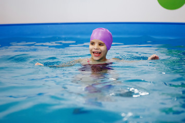 Girl in the lilac hat is having fun, swimming in the pool.
