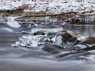 smooth motion of wild water in a river in winter with snow and ice on rocks and stones in the beautiful nature of a forest