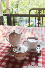 A cup of tea with a teapot on the table. A Cup of freshly brewed black tea,escaping steam,warm soft light.