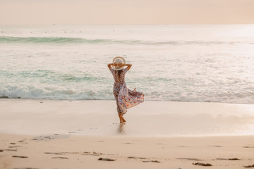 Attractive woman in summer dress on beach at sunset or sunrise. Feminine style.