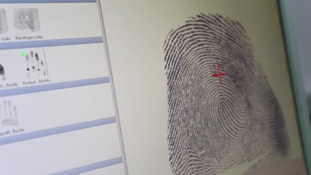 A police officer takes a suspect's fingerprints on a digital device. The fingerprint is shown on a computer screen.