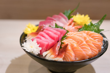 Mixed sliced fish sashimi on ice in black bowl. Sashimi Salmon Tuna Hamachi Prawn and Surf Calm set, raw fish, japanese food in Asian restaurant.