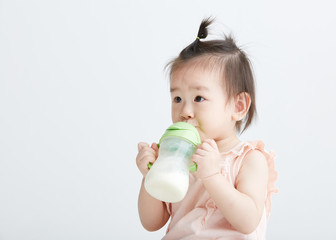 Cute Asian girl drinking milk with a bottle. On white background