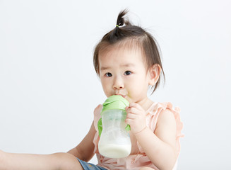 Cute Asian girl drinking milk with a bottle. On white background