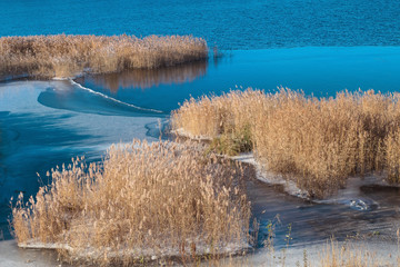 First ice on blue water. Late autumn landscape with yellow thickets of reeds in a cold river.