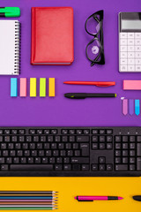 Modern working place with keyboard, diary, pencils, pens and glasses on orange-purple background. Top view