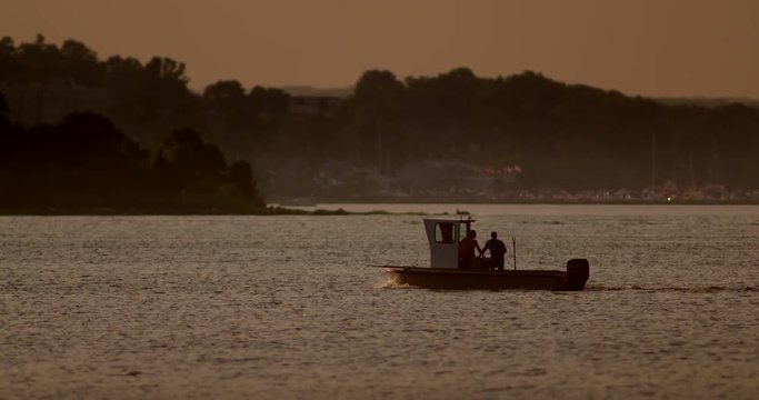 Silhouetted fishing boat moves through harbor in slow motion