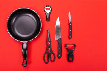 Frying pan with kitchen utensils isolated on red background