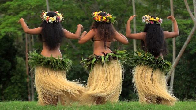 Polynesian girls in grass skirts and flower headdress dancing hula style while entertaining barefoot outdoors Tahiti French Polynesia 