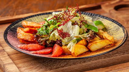 Modern Arabic cuisine in 2019. Asian salad of fried salmon, avacado, grapefruit and salad mix, with honey sauce. Serving dishes in a restaurant in a black plate with oriental spices.