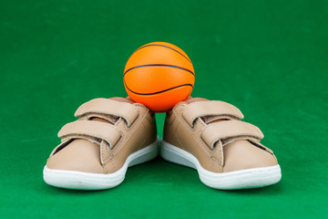 Concept encourage children to play sport, exercise for a healthy body, shoes of small baby shoes next to ball isolated on green background.