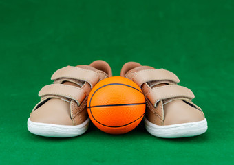 Concept encourage children to play sport, exercise for a healthy body, shoes of small baby shoes next to ball isolated on green background.