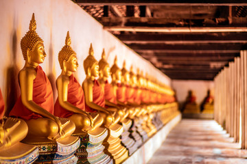 Row of golden meditation buddha sitting figures statues inside corridor  is lined up at Wat...