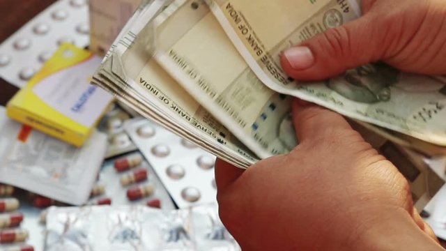 Close up of male hand Counting Indian rupee notes over Pile of pharmaceutical drug, medicine pills and Indian money, cost of healthcare and medical