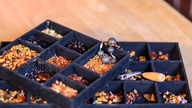 A black tray for handcrafting with multiple sections filled with various kinds of amber and tools for crafting