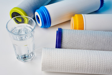 Water filters. Carbon cartridges and a glass on a white background. Household filtration system.