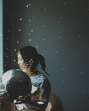 Thoughtful young woman with disco ball looking through window