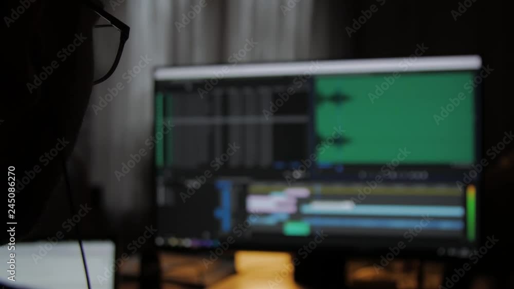 Poster young man using computer, editing a video in editing software, shot from behind.
