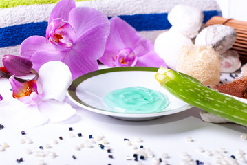 A set up of wellness items, a candle, stones, a beauty sponge, a sea star, towel, flowers, a natural sponge, aloe vera leave, aloe vera gel, wood, a bamboo mat, decorative stones, a colorful drink