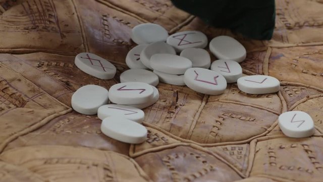 Woman's hands collect a small set of white rune-stones into a pouch