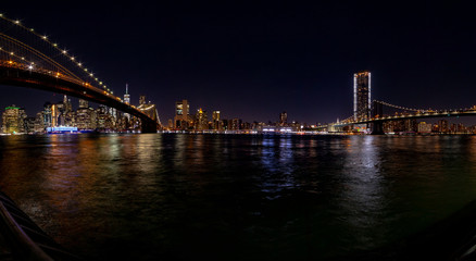 New York at night. Stitched panorama of a lower Manhattan from Empire Fulton Ferry park with Brooklyn and Manhattan bridges.