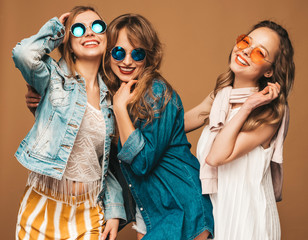 Three young beautiful smiling hipster girls in trendy summer casual clothes. Sexy carefree women posing near blue wall. Positive models going crazy. Showing peace sign and winking