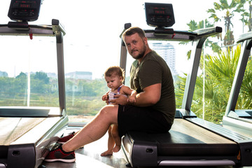 Young father and little cute daughter in the gym on a treadmill.