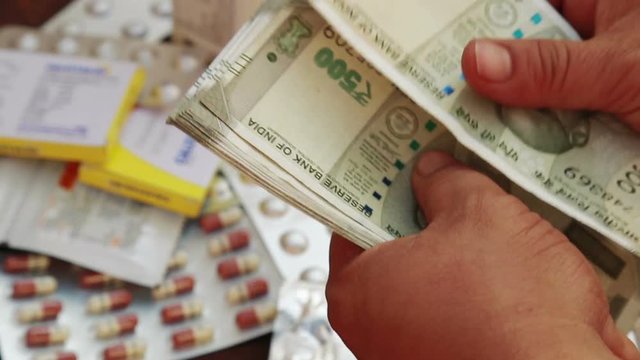 Close up of male hand Counting Indian rupee notes over Pile of pharmaceutical drug, medicine pills and Indian money, cost of healthcare and medical