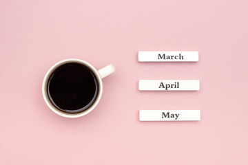 Wooden calendar spring months March April May and Cup of black coffee directed at March on pastel pink paper background. Concept Hello March Creative Top view Flat Lay Greeting card