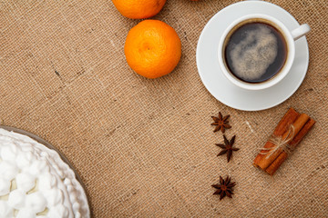Biscuit cake decorated with whipped cream, cup of coffee, oranges, star anise and cinnamon