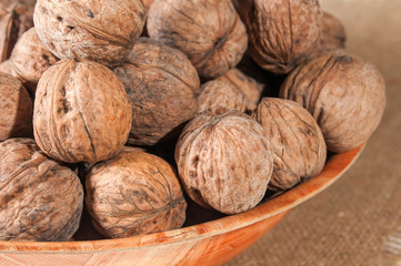 Many walnuts lie in a bowl. Bowl on burlap. Close-up.