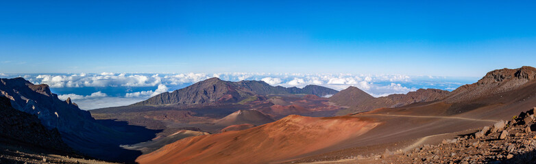 Fototapeta na wymiar Scenic panorama of a Haleakala volcano from Keonehe'ehe'e trail overlooking cinder cones inside a caldera. Clear blue sky white puffy clouds below the horizon and rich red-brown colors of a mountain