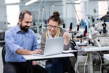 Businessman and fashion designer working on computer in textile factory