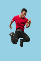 always on mobile. Full length of handsome african young man taking phone while jumping against blue studio background. Mobile, motion, movement, business concepts