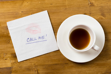 Napkin with a kiss and coffee cup on wooden background.
