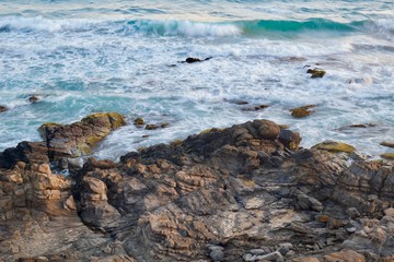High angle photo of blurred waves crashing onto sunlit rocks