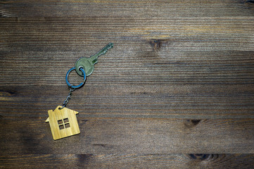 Fototapeta na wymiar The symbol of the house in the form of a keychain with a metal key on a brown vintage wooden background. Copy space.
