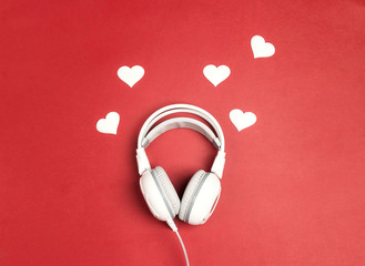 White headphones with heart on red background. Romantic music concept.