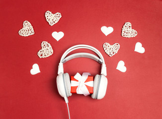 White headphones with gift box and decorative hearts on a red background. St. Valentines Day music...