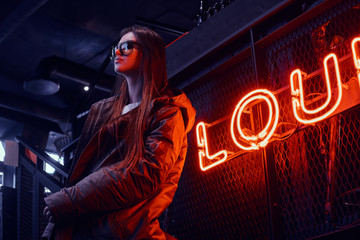 Young stylish girl wearing a hoodie coat and sunglasses standing on stairs at underground nightclub...