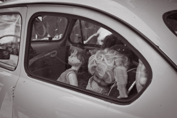 Old dolls in the back seat of a car. View through the window. Monochrome image.