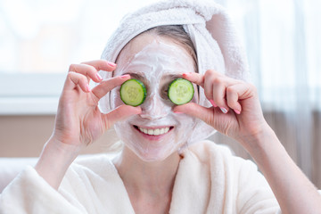 Beautiful young woman with natural cosmetic mask and cucumber slices on her face. Skin care and Spa treatments at home