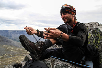 A young white Caucasian man with a slight unshavenness is preparing for a new day of hiking in the...