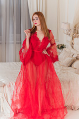 Sensual red hair woman in a red lace boudoir dress on a bed in a vintage pastel bedroom, lingerie red color 