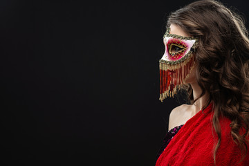 Young woman wearing venetian carnival mask  against black background sideway. Place for text