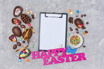 Mock up of clipboard with pink text of happy easter and chocolate traditional eggs.