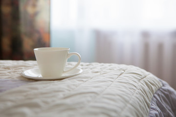 Morning cup of coffee on the background of the bed and the window
