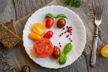 Mixed tomatoes of different colours with herbs and oil on white plate