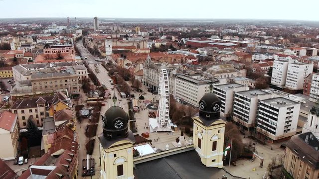 Aerial shot flying over the Reformed Great Church of Debrecen, with a large ferris wheel in the main square below during Christmas